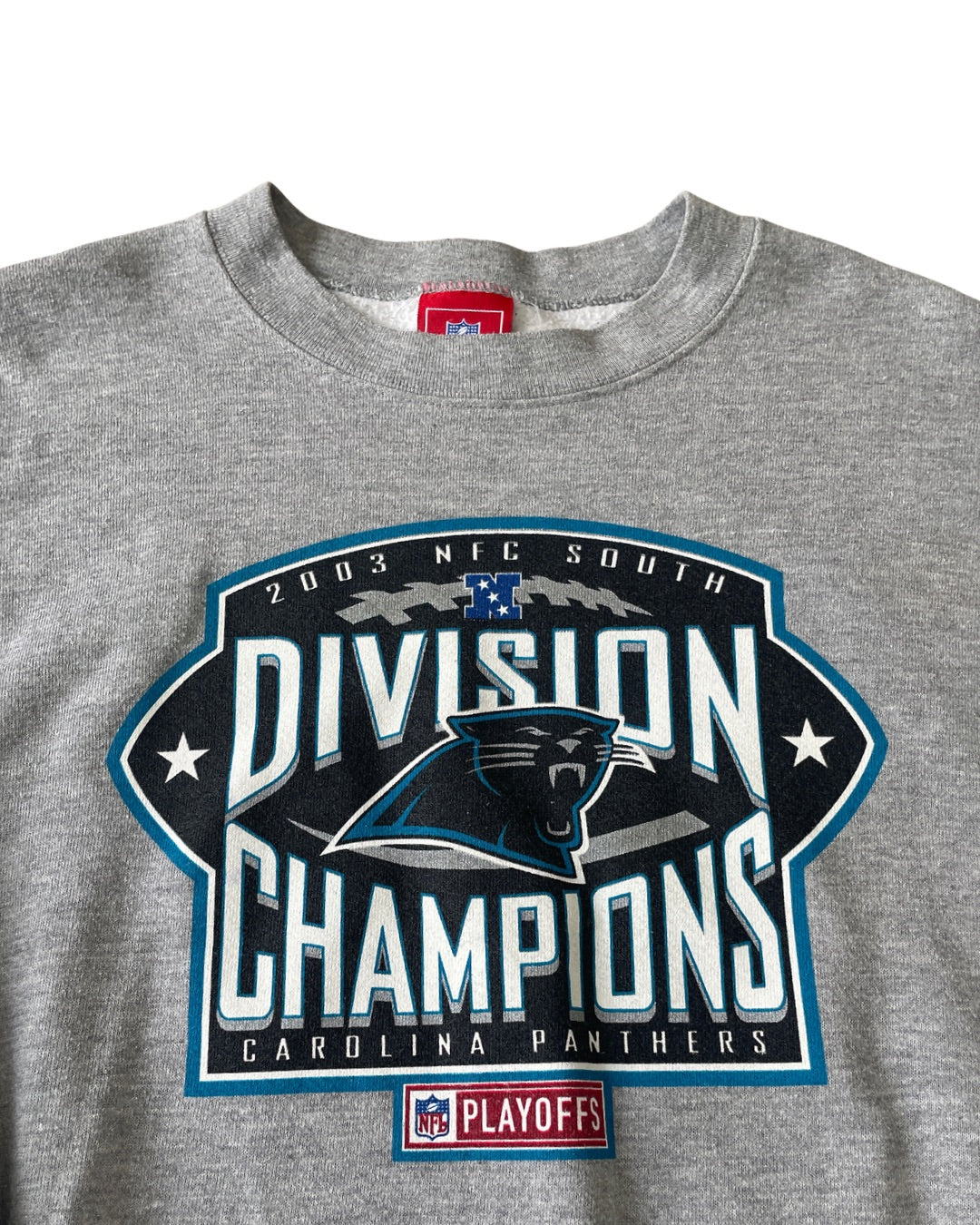 A close-up of a heather gray crewneck sweatshirt featuring a large graphic print for the Carolina Panthers 2003 NFC South Division Champions. The graphic includes the Carolina Panthers logo, 'DIVISION CHAMPIONS' in bold white letters, and an NFL Playoffs patch below.