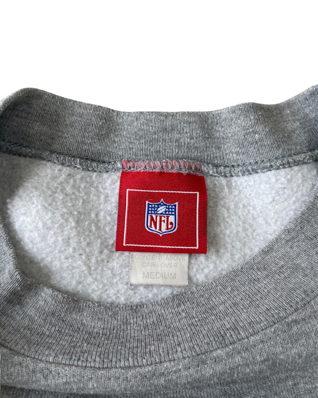 Close-up of the inside neck of a gray crewneck sweatshirt, showing a red NFL brand tag sewn onto a white fleece lining.
