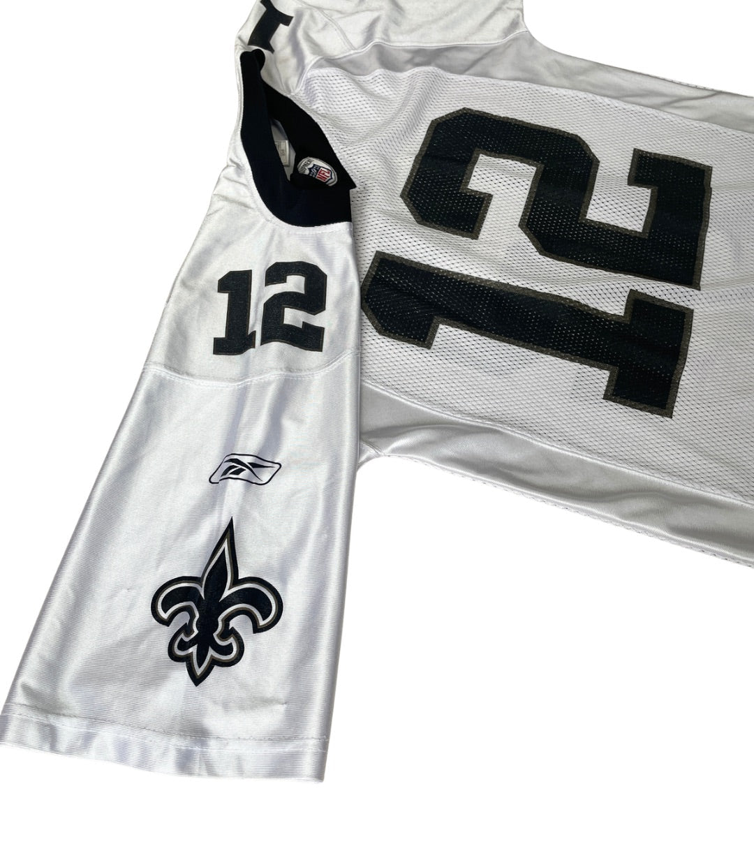 A white New Orleans Saints football jersey with black numbers and logos, laid flat on a white background. The jersey shows the number 12 on the sleeve and 21 on the back, with the Saints fleur-de-lis logo on the front.