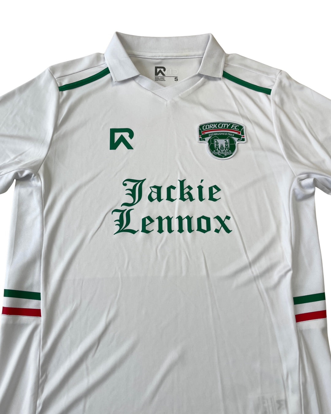 A white short-sleeve football jersey with green and red accents, featuring the 'Cushion City FC' crest on the left chest, a green stylized 'R' logo on the right chest, and 'Jackie Lennox' printed in green across the center.